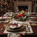 Dining table set for Christmas with candles, glasses, and place settings.