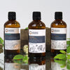 Three bottles of Ancient Wisdom essential oils on a reflective surface with greenery.