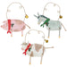 Three rustic Christmas animal ornaments hanging from wire loops: a pink-and-white pig with a red polka-dot scarf, a pale blue-gray donkey with a green scarf, and a white-and-tan cow with a red scarf, each with a small gold bell.