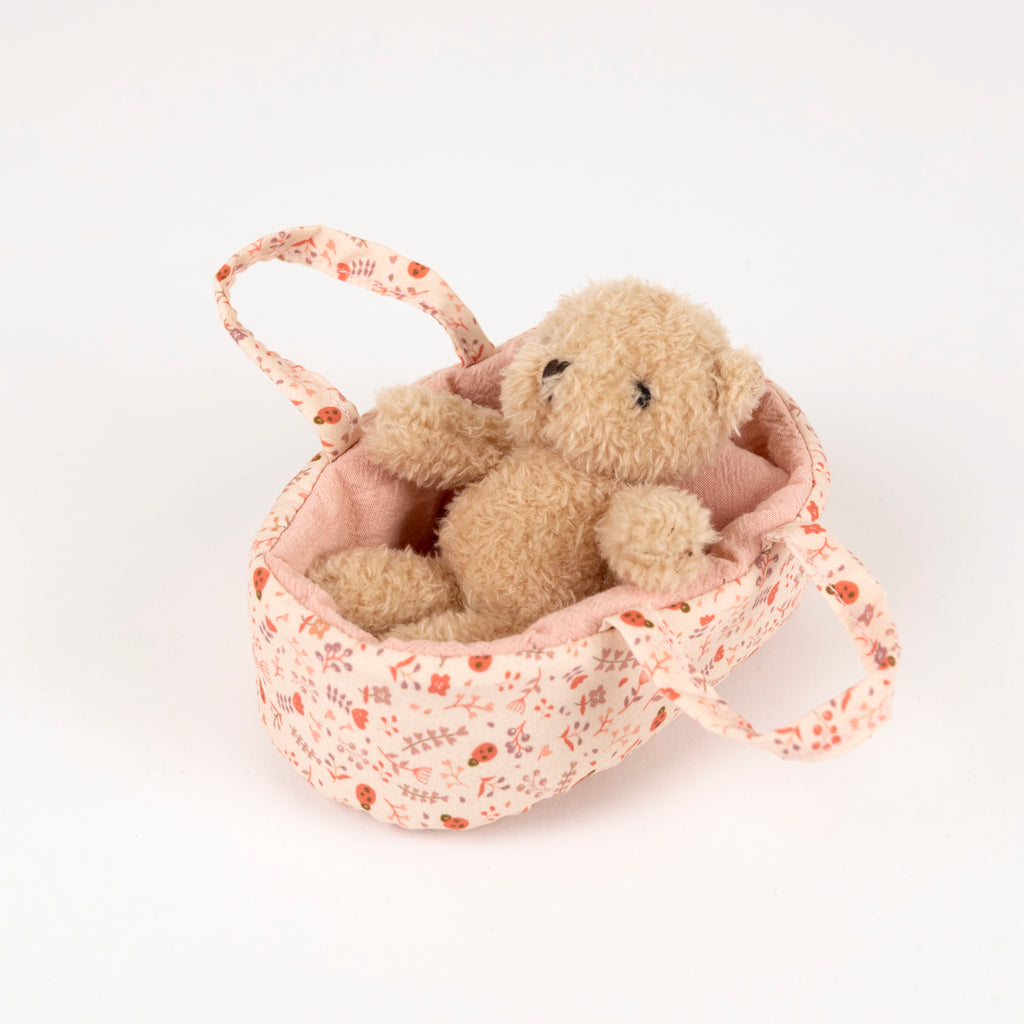 Small teddy bear in a floral-patterned basket on a white background