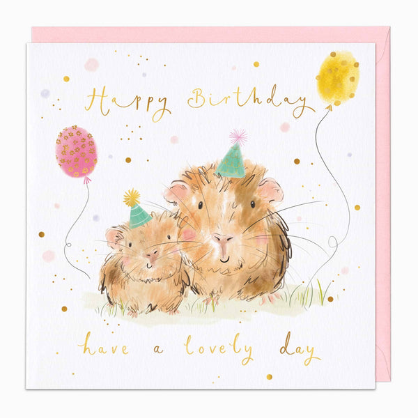 A square birthday card with a white front and a pale pink envelope behind it. The card features a watercolor illustration of two brown guinea pigs wearing party hats, with gold script text reading 'Happy Birthday' and 'have a lovely day,' plus small gold and pink polka-dot balloon accents.