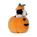 A plush toy dog wearing an orange pumpkin hat with green leaves, sitting inside a matching orange pumpkin bed with a black stitched face, on a plain white background.