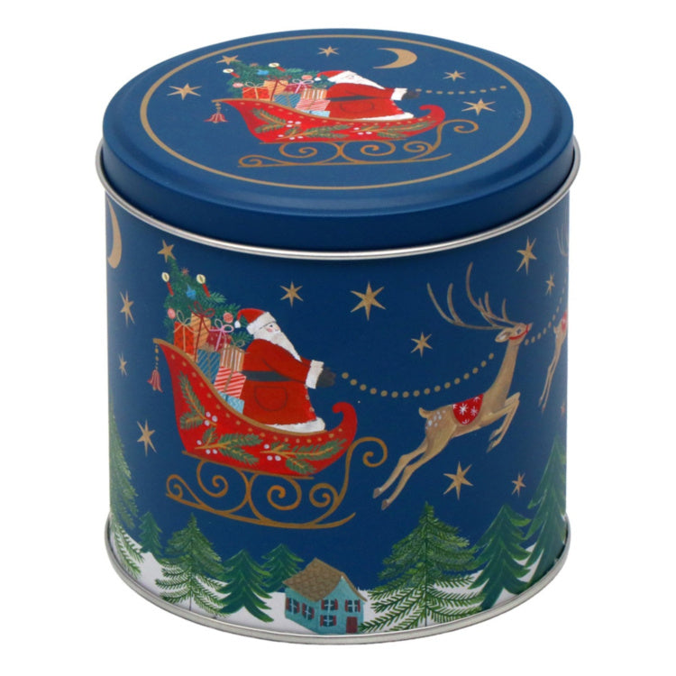A round metal tin with a festive Christmas design featuring Santa Claus in a sleigh, a reindeer, stars, trees, and a small house on a dark blue background.
