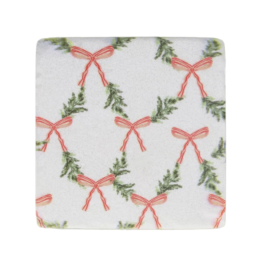 A square white fabric napkin or coaster with a repeating pattern of green pine garlands and coral-red ribbon bows, shown flat against a white background.