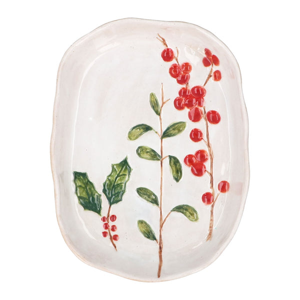 An oval ceramic serving platter with a white glaze, decorated with painted holly leaves and red berries.