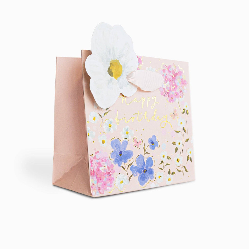 Gift bag with floral design and a white flower on a white background