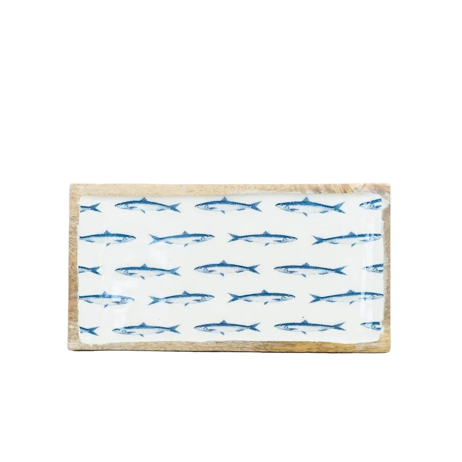 A rectangular wooden serving board with a white top printed with rows of blue fish, set on a light wood tabletop against a white background.