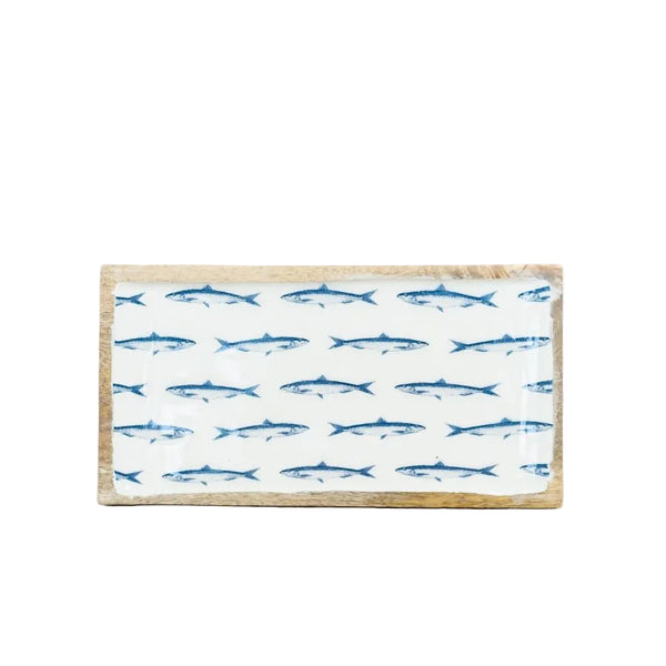A rectangular wooden serving board with a white top printed with rows of blue fish, set on a light wood tabletop against a white background.
