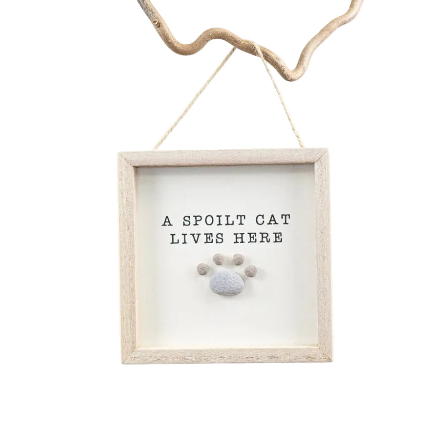 Decorative sign with 'A spoilt cat lives here' text and paw print design, hanging on a white background