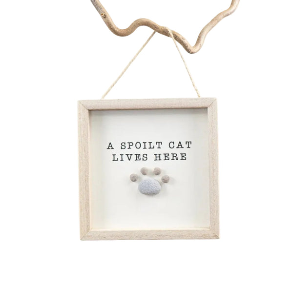 Decorative sign with 'A spoilt cat lives here' text and paw print design, hanging on a white background
