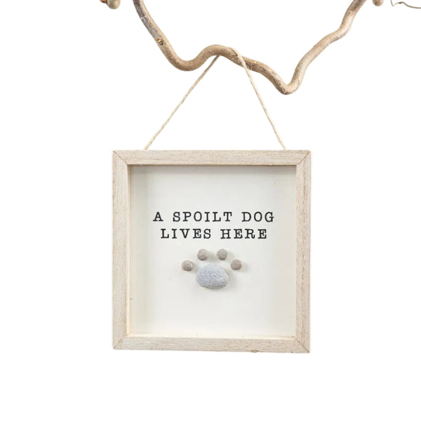 Decorative sign with 'A Spoilt Dog Lives Here' text and paw print in a wooden frame, hanging on a branch.