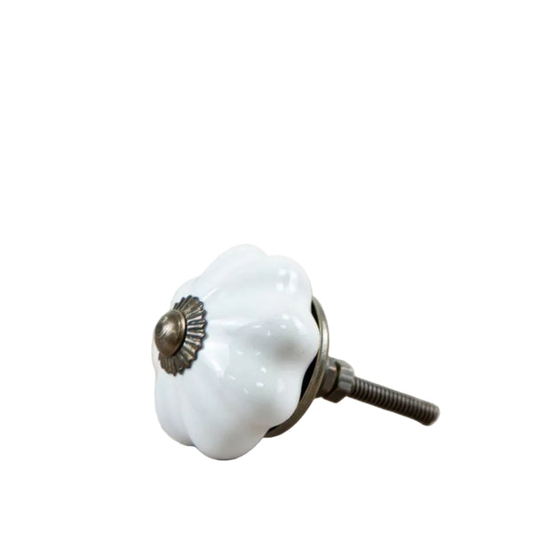 A single white ceramic drawer knob with a ribbed flower-like shape and an antique bronze metal screw base, resting on a light wood surface.