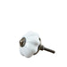 A single white ceramic drawer knob with a ribbed flower-like shape and an antique bronze metal screw base, resting on a light wood surface.