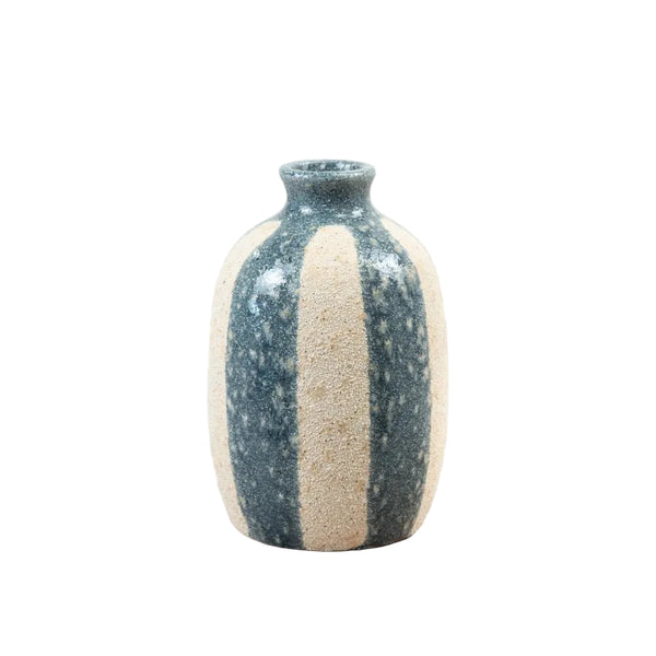 A small handmade ceramic bottle with a dark speckled glaze and a vertical beige stripe, sitting on a light wooden surface against a white background.