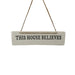 A white rectangular hanging sign with the phrase 'THIS HOUSE BELIEVES' in black lettering, suspended by twine from a wooden trim against a white background