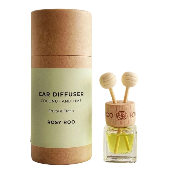 A car diffuser set by Rosy Roo, featuring a cylindrical kraft paper tube with a pale green label next to a small glass bottle with yellow liquid and two wooden diffuser sticks, set on a light surface with a blurred vase in the background.
