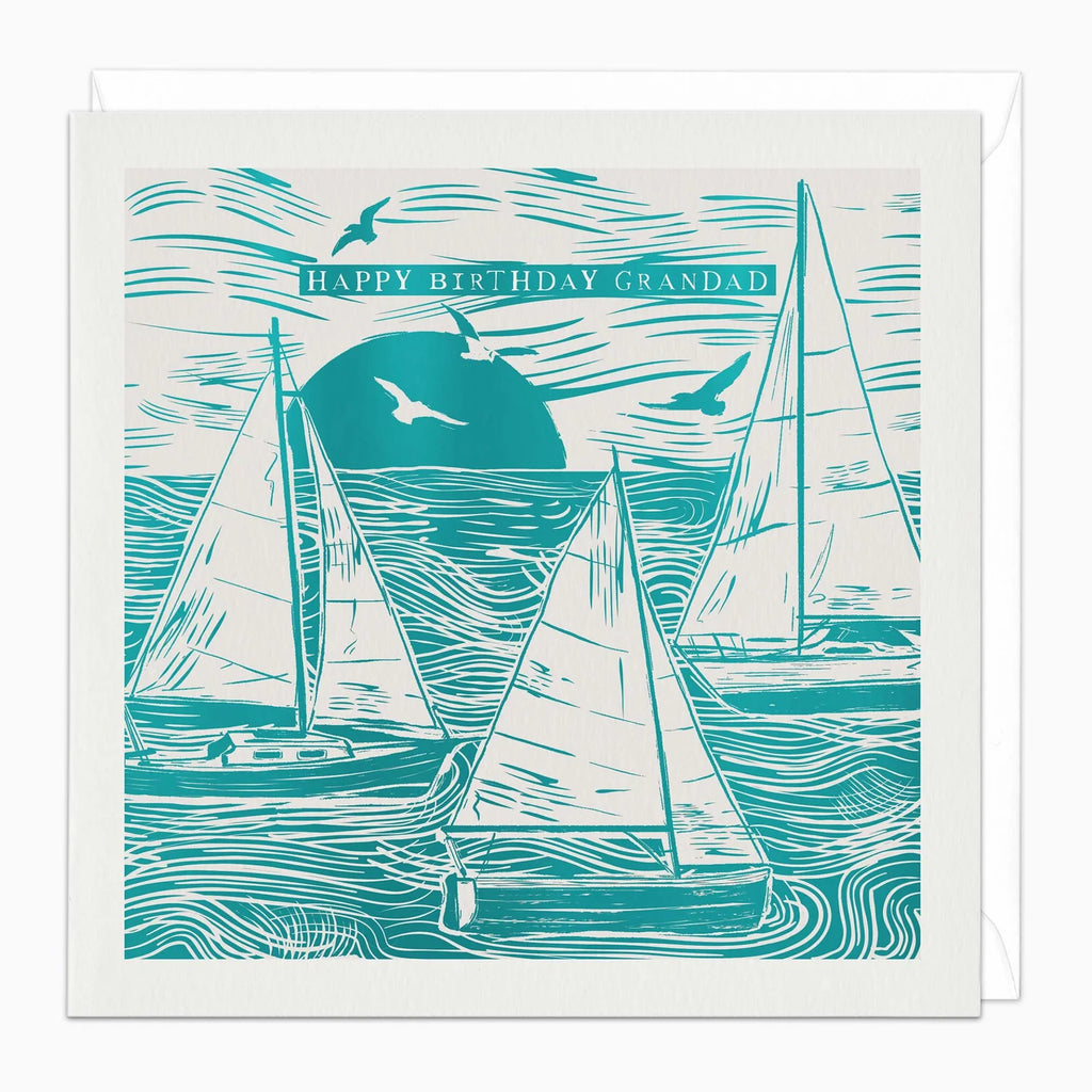 A square birthday card with a white envelope behind it, featuring a teal and off-white woodcut-style illustration of sailboats on the water with birds and the text 'HAPPY BIRTHDAY GRANDAD'.