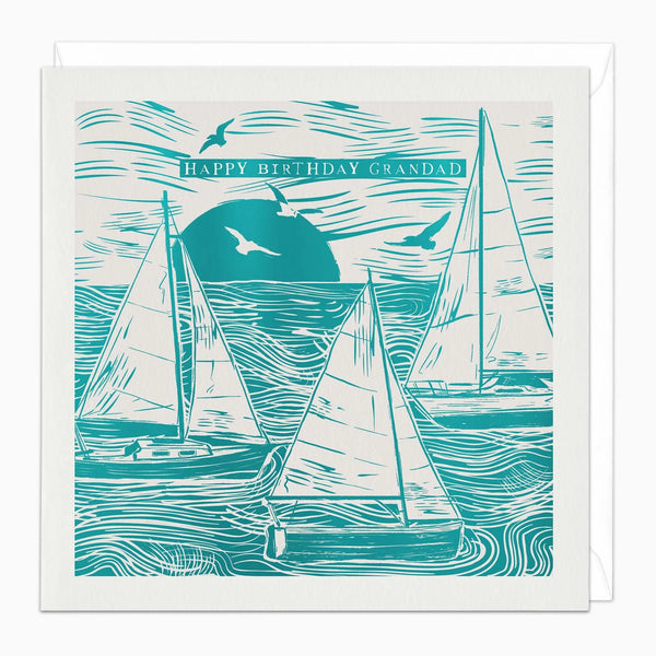 A square birthday card with a white envelope behind it, featuring a teal and off-white woodcut-style illustration of sailboats on the water with birds and the text 'HAPPY BIRTHDAY GRANDAD'.