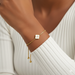 Gold bracelet with a clover charm on a wrist against a white background