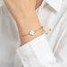 Gold bracelet with a heart charm on a person wearing a white shirt.