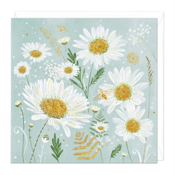 A square art print or card featuring a botanical illustration of white daisies with yellow centers, green leaves, small bees, and delicate wildflowers on a pale blue background, with a white envelope partially visible behind it.