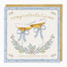 A square congratulations greeting card with a light blue border, gold script text reading 'congratulations' and 'WHAT WONDERFUL NEWS,' and an illustration of two champagne glasses tied with pale blue bows, shown with a gold envelope behind it.