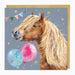 A square greeting card featuring a painted brown horse with a long blonde mane, set against a dusty blue-gray background with colorful balloons and stars. A gold envelope is partially visible behind the card.