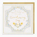 A square Christening Day greeting card with a gold envelope behind it. The card has a white background with a decorative floral border in blue, yellow, and green, and gold text reading 'To a very special little one on your Christening Day'.
