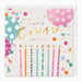 A square birthday card with a white background and colorful balloon and candle illustrations. The text reads 'to a lovely cousin on your birthday' in playful multicolor lettering, with pink, teal, orange, and gold accents.