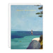 A square birthday card with a white envelope behind it, featuring an illustrated beach scene with a person hanging from a swing over the ocean and the text 'HAPPY BIRTHDAY' in gold at the top.