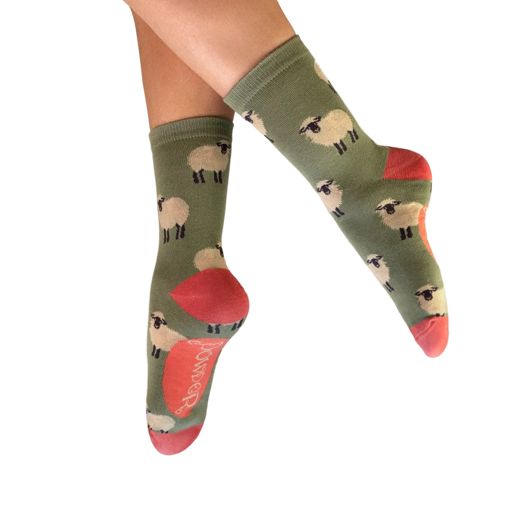 Green socks with sheep pattern worn by a person on a white background