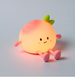 Night Light Toy resembling an peach with a smiling face on a grey background.
