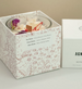 Candle in a decorative box with floral design and brand name on a neutral background