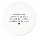 A porcelain coaster featuring a hand-stamped, typewriter-style font with the quote: "Motherhood powered by love fueled by coffee sustained by wine," finished with a small black heart at the bottom on a white background.
