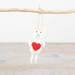 White plush toy with a red heart on a wooden branch against a textured background