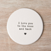 Round white ceramic coaster with 'I love you to the moon and back' text on a wooden surface