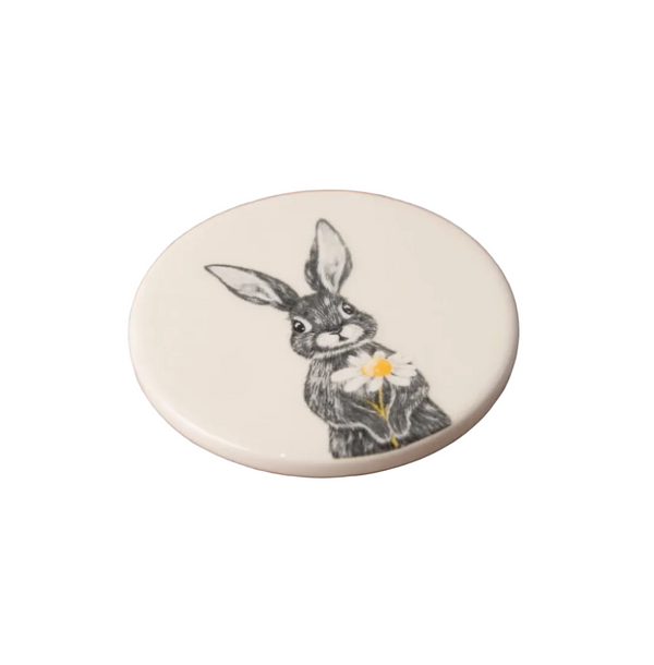 Round ceramic coaster with a rabbit illustration holding a flower on a white background
