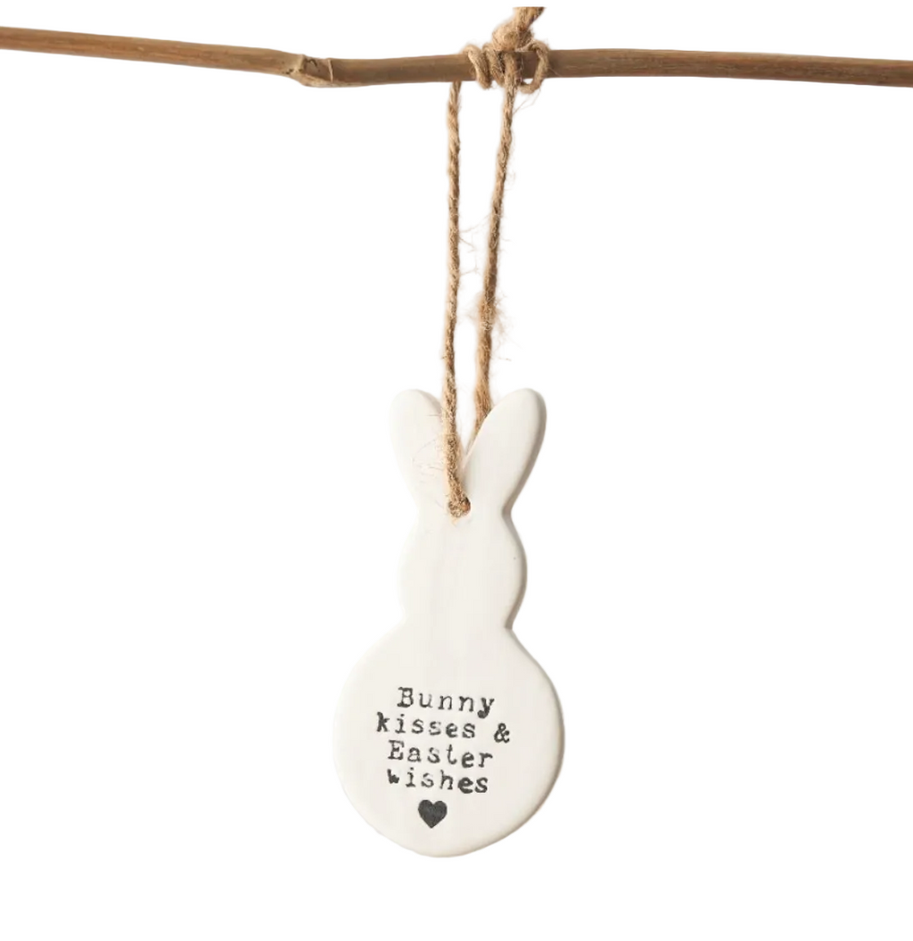White ceramic bunny ornament with text hanging on a branch against a white background