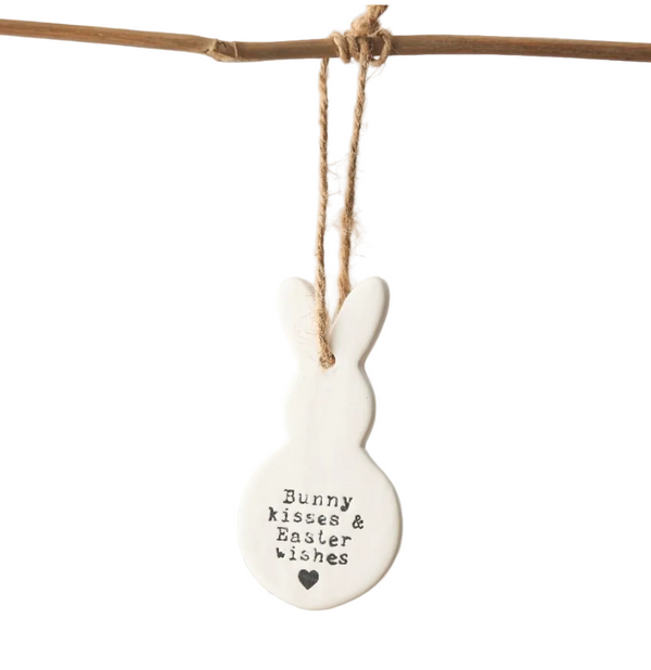 White ceramic bunny ornament with text hanging on a branch against a white background
