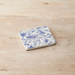 Ceramic coaster with blue floral and animal pattern on a wooden background