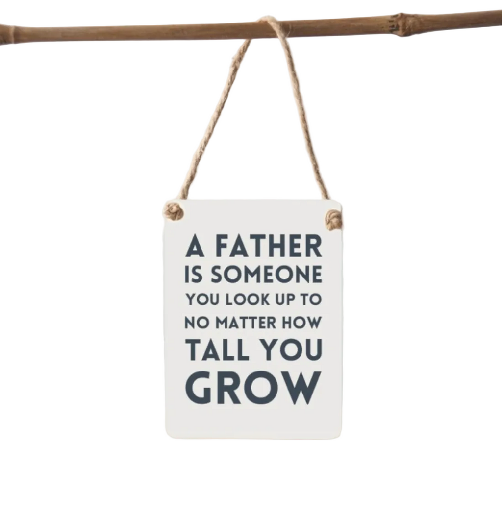 Decorative sign with a motivational quote about fathers hanging on a branch.