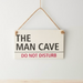Decorative sign with 'The Man Cave Do Not Disturb' text on a plain background