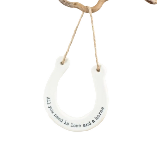 Round white sign with text 'All you need is love and a horse' hanging on a white surface.
