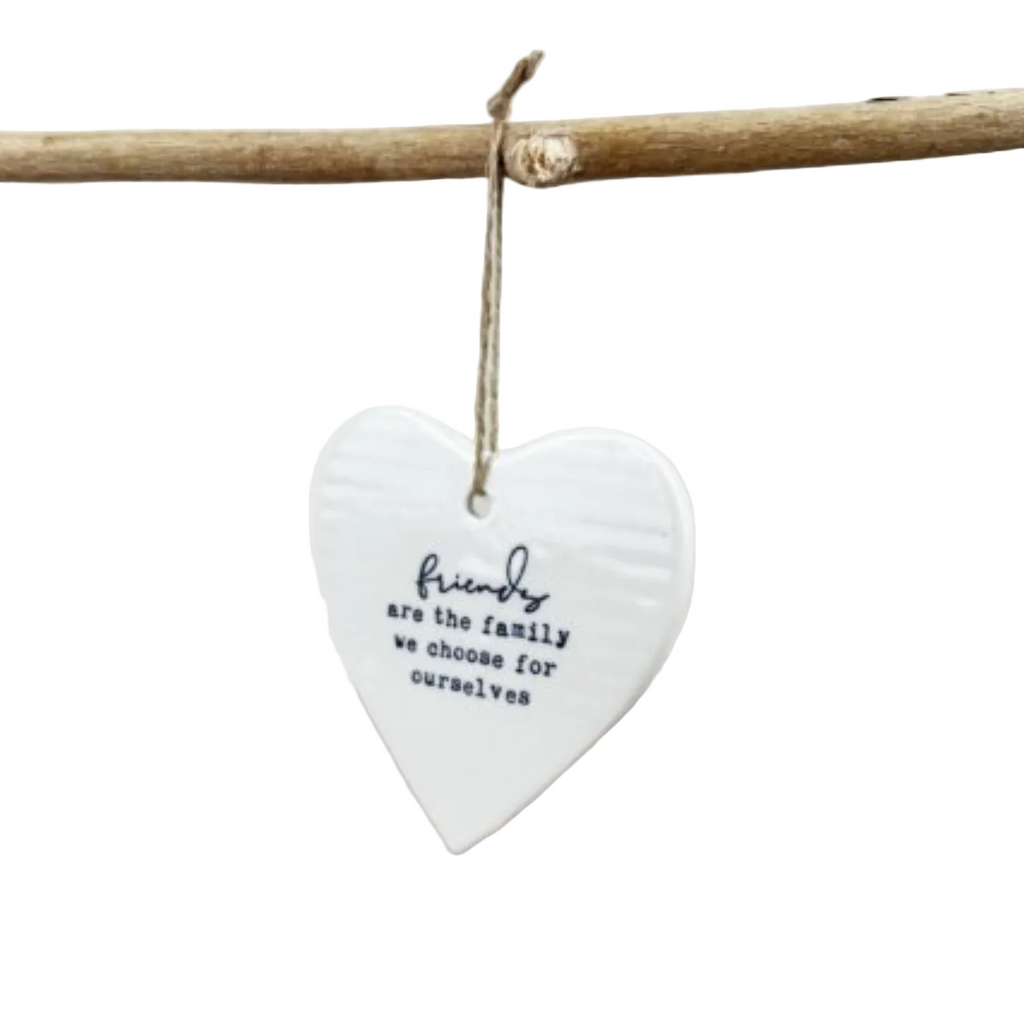 White heart-shaped hanging ornament with text on a branch against a light background