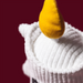 A close-up of a white ribbed plush or fleece garment with a yellow teardrop-shaped accent on top, photographed against a solid dark red background.