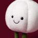A close-up of a white knitted garlic-shaped plush toy with embroidered black eyes and a smile, set against a solid dark red background.