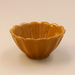 A small glossy ceramic bowl with a scalloped, petal-like rim, shown on a plain light beige background.