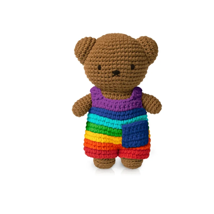 A crocheted teddy bear toy wearing a rainbow-striped shirt and shorts, centered on a plain white background.