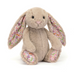 A plush stuffed bunny in warm beige with long floppy ears and floral-patterned inner ears, photographed on a clean white background.