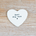 A white heart-shaped ceramic plaque with the text 'Best dog mum' and a small heart printed in black, displayed on a light-colored wooden surface.